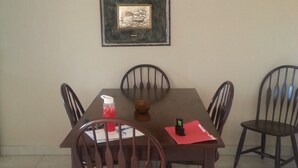 Un coin repas avec une table et des chaises, un ventilateur de plafond, un tableau encadré au mur et un sol carrelé.