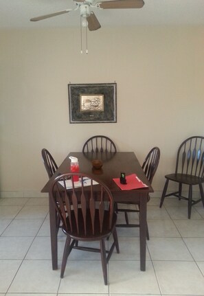 Un comedor con una mesa y sillas, un ventilador de techo, un cuadro en la pared y piso de baldosas.