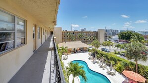 Un balcon d’hôtel avec vue sur une piscine, un espace de détente extérieur et un parking.