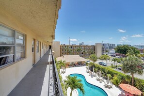 Een hotelbalkon met uitzicht op een zwembad, zitplaatsen buiten en een parkeerplaats.