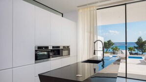 Una cocina moderna con electrodomésticos integrados, un ventanal grande y vistas a una piscina y al océano.