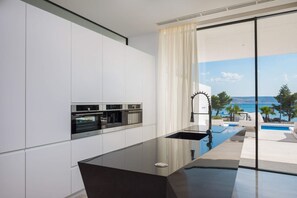 Eine moderne Küche mit eingebauten Geräten, einem großen Fenster und Blick auf Pool und Meer.