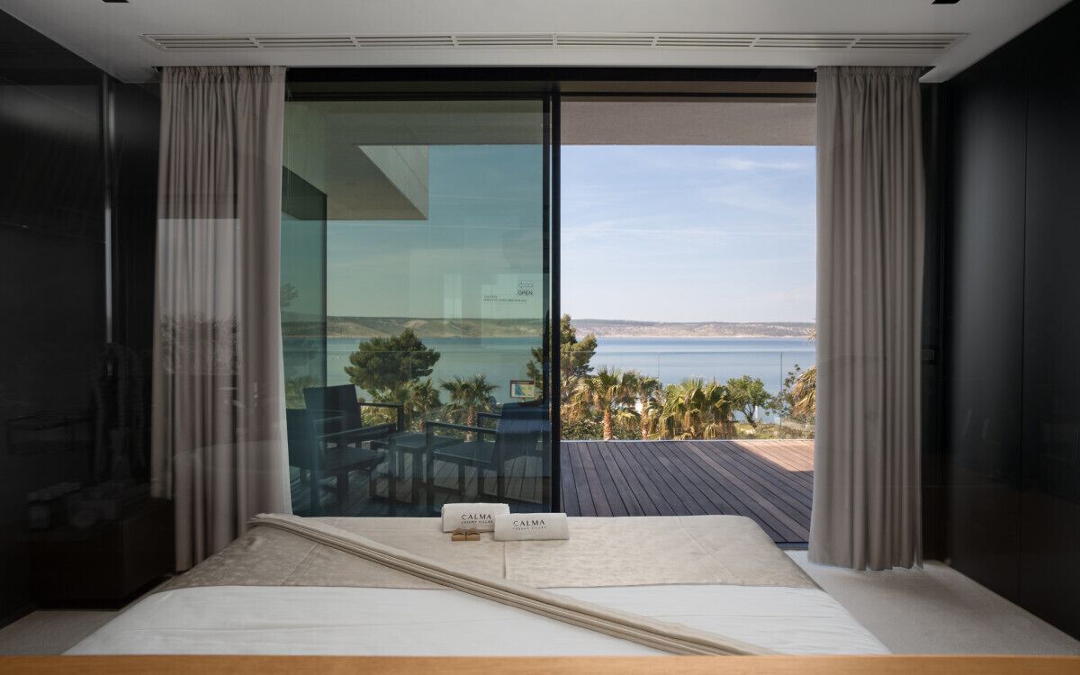 Une chambre dotée d’une grande porte-fenêtre coulissante donnant sur un balcon avec vue sur la mer.