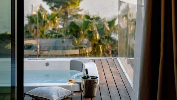 Un balcón con un jacuzzi, una mesa de vidrio, un cojín y una copa de vino.