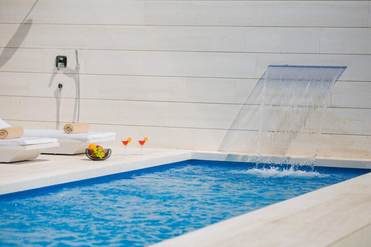 A pool with a water feature, lounge chairs, and a fruit bowl.