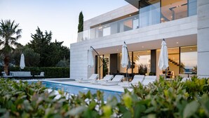 Una casa moderna con piscina, sillas de descanso y sombrillas.