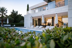 Ein modernes Haus mit Swimmingpool, Liegestühlen und Sonnenschirmen.