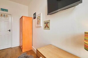 Ein Zimmer mit Fernseher, einem Holzkasten, einem gerahmten Bild und einem kleinen Holztisch.
