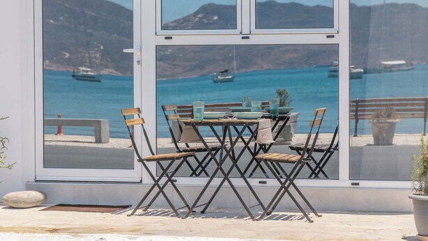 A table and chairs set up near a large window overlooking a coastal area with boats. - Akti Waterfront Modern Lofts: Pelagos (Adamantas Milos)