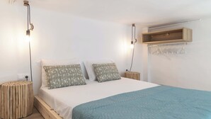 A bedroom with a bed, two bedside tables, a hanging light, and a wooden shelf. - Akti Waterfront Modern Lofts: Pelagos (Adamantas Milos)