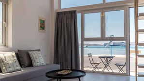 A modern room with a sofa, a small round table, and a view of the sea through large windows. - Akti Waterfront Modern Lofts: Pelagos (Adamantas Milos)