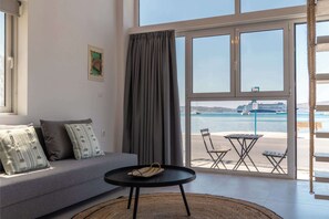 A modern room with a sofa, a small round table, and a view of the sea through large windows.