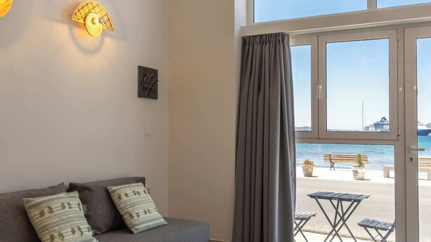 Ein Wohnzimmer mit einer Couch, einem runden Couchtisch, einer hängenden Leuchte und Meerblick durch große Fenster.