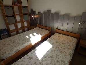 Une chambre à coucher avec deux lits en bois, une armoire en bois et une étagère avec des boîtes de rangement.