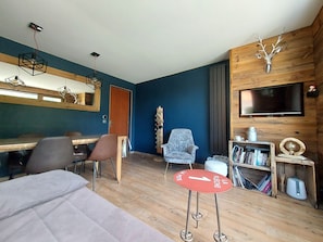 A modern room with a wooden floor, a dining table, a sofa, a TV mounted on the wall, and a bookshelf.