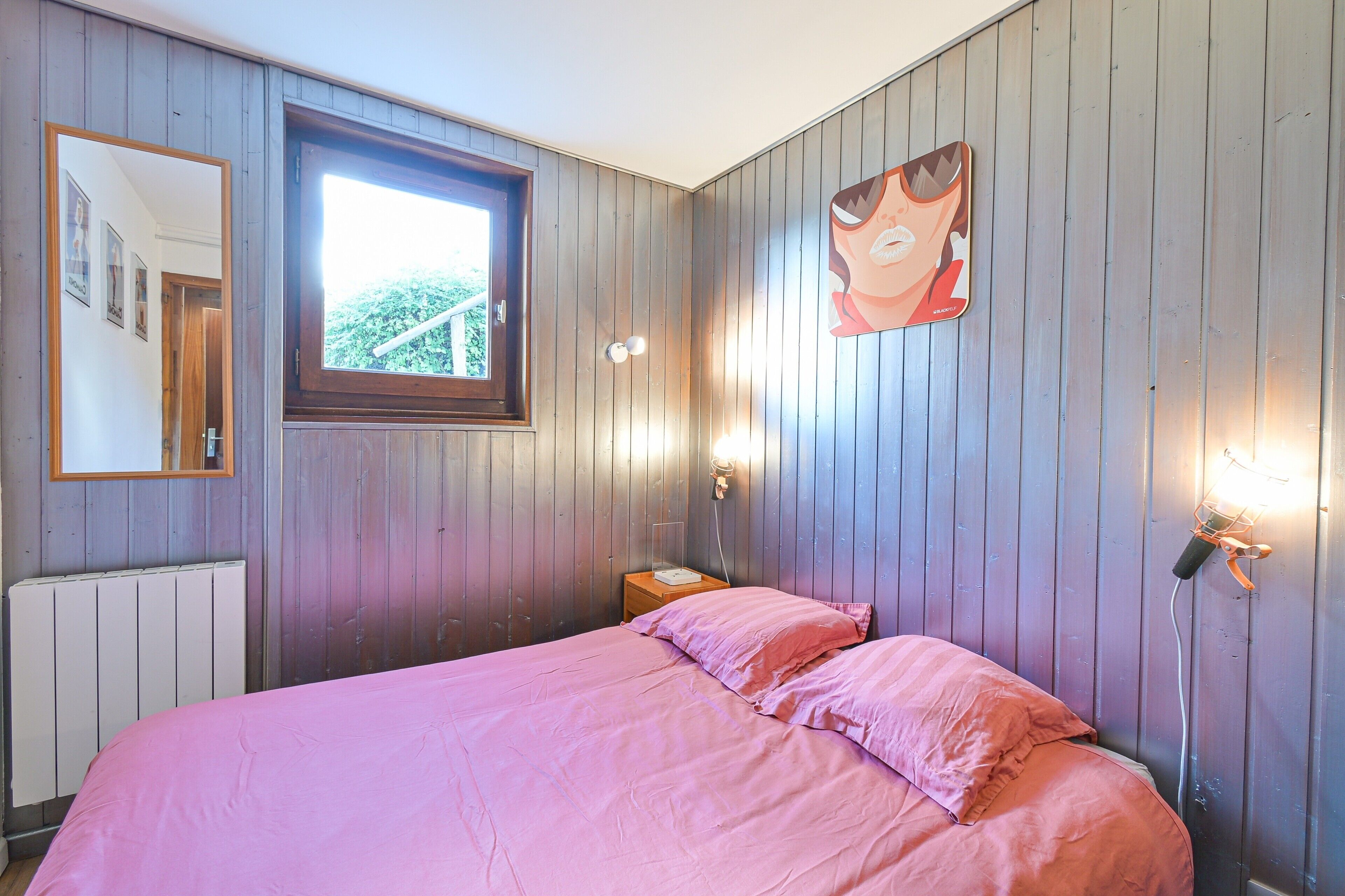 Un dormitorio con cama, ventana, lámpara de pared y un cartel.