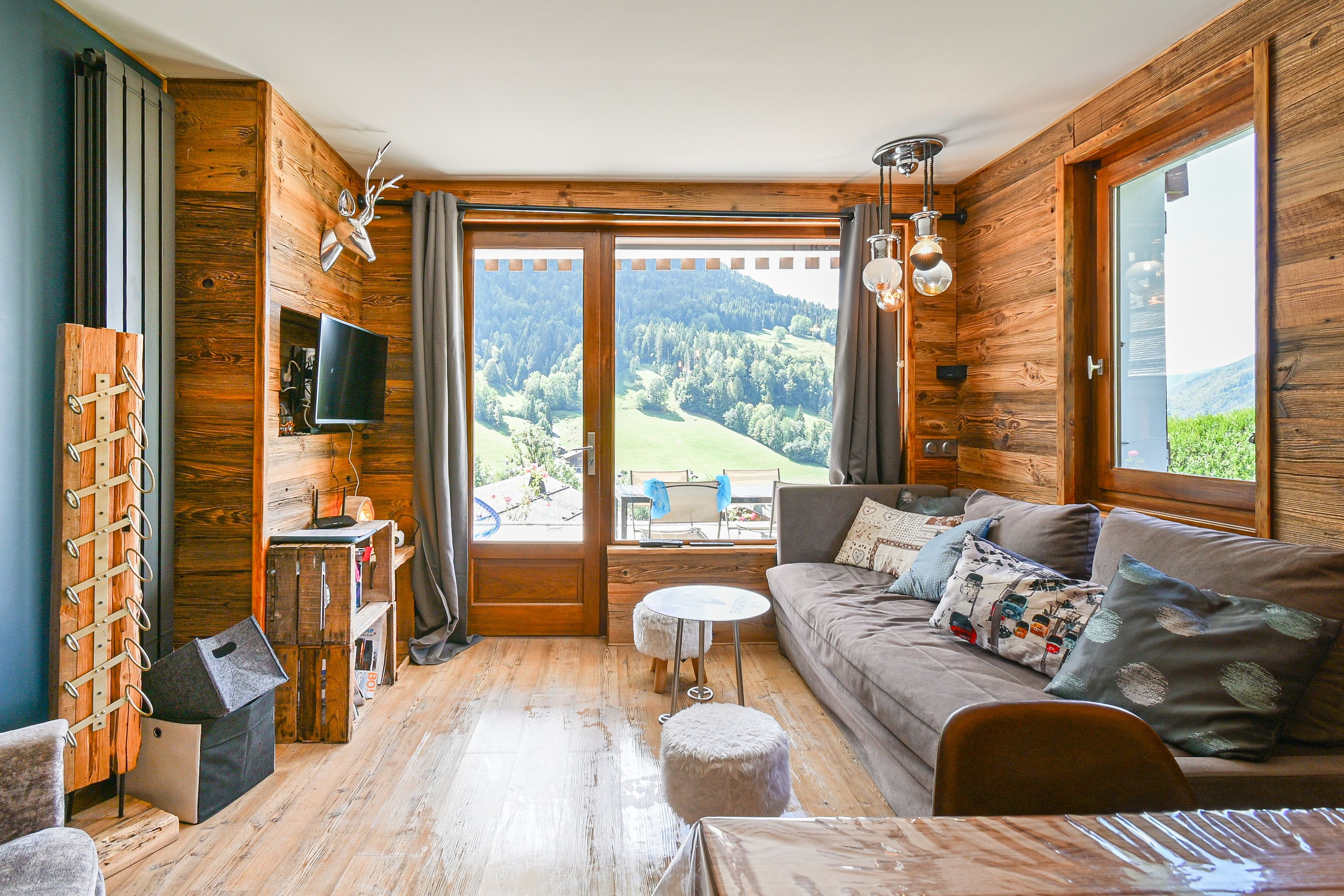 L’intérieur d’un chalet accueillant, avec un décor en bois, un canapé, un téléviseur et une vue sur un paysage boisé.