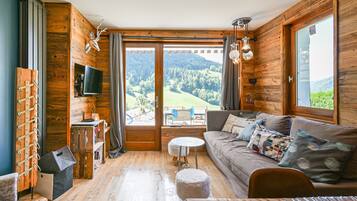 A cozy cabin interior with a wooden interior, a sofa, a television, and a view of a forested landscape.