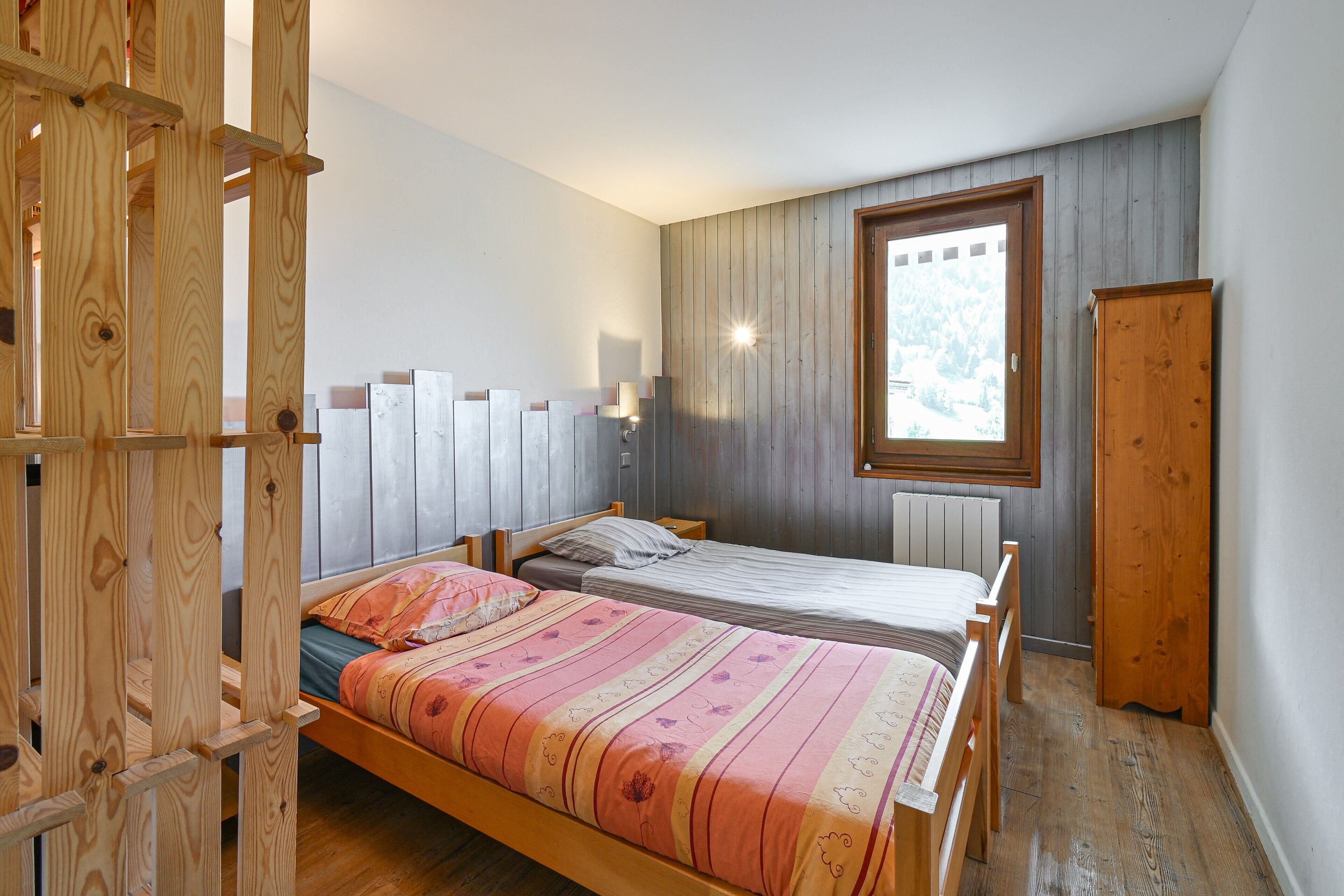Ein Schlafzimmer mit zwei Betten, einem Holzschrank, einem Fenster mit Blick und einer Holzleiter.