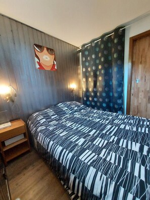 A bedroom with a bed, a nightstand, a wall-mounted lamp, and a door with a curtain.