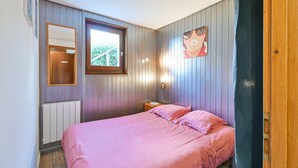 Et soveværelse med seng, et vindue, en radiator, et natbord og en lampe på væggen.