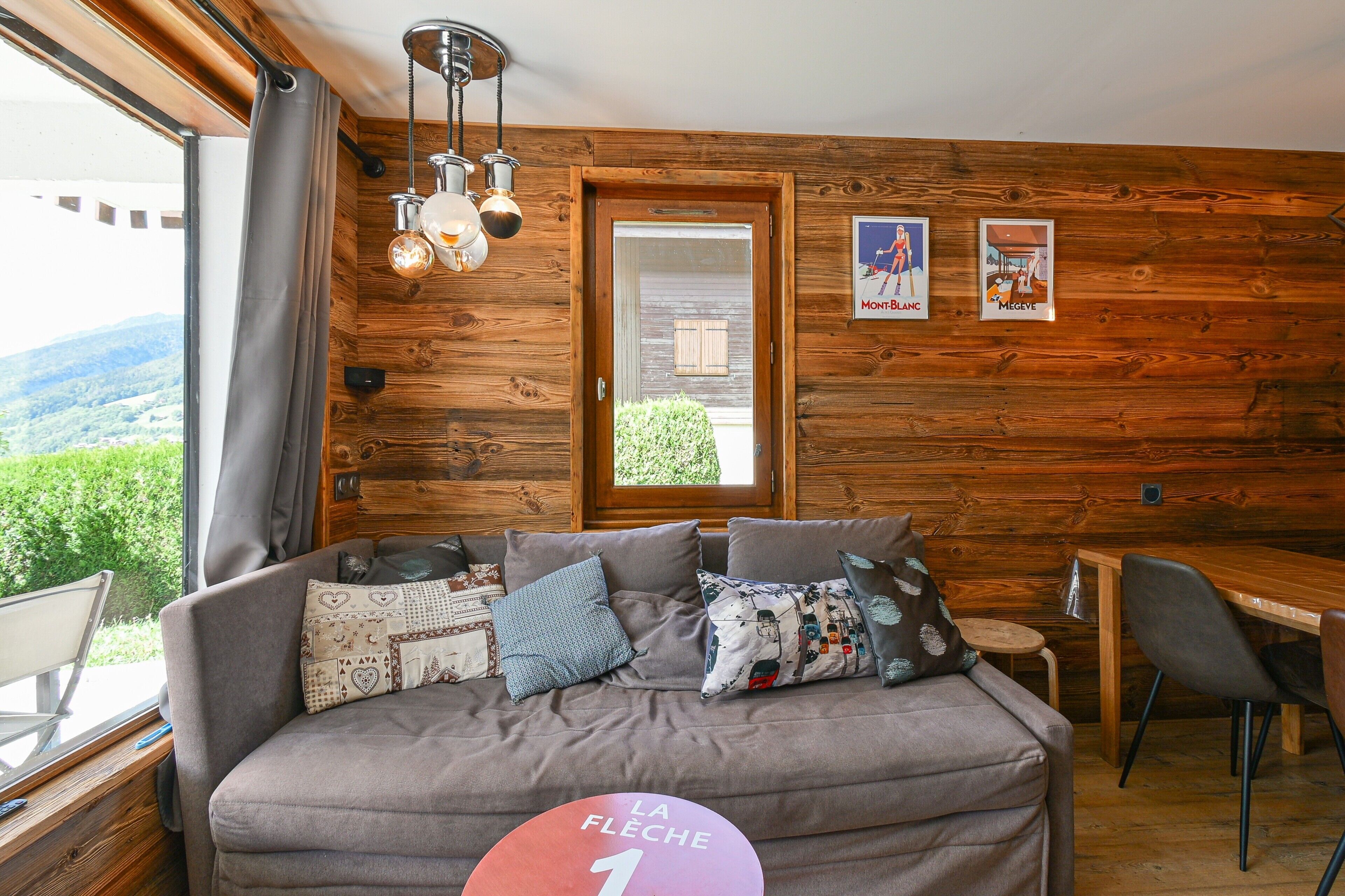 Una habitación acogedora con detalles de madera, un sofá con cojines estampados, una mesa de comedor y vistas al exterior.