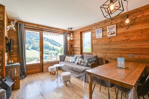 Een gezellige kamer met houten wanden, een bank, een eettafel en uitzicht op het landschap.