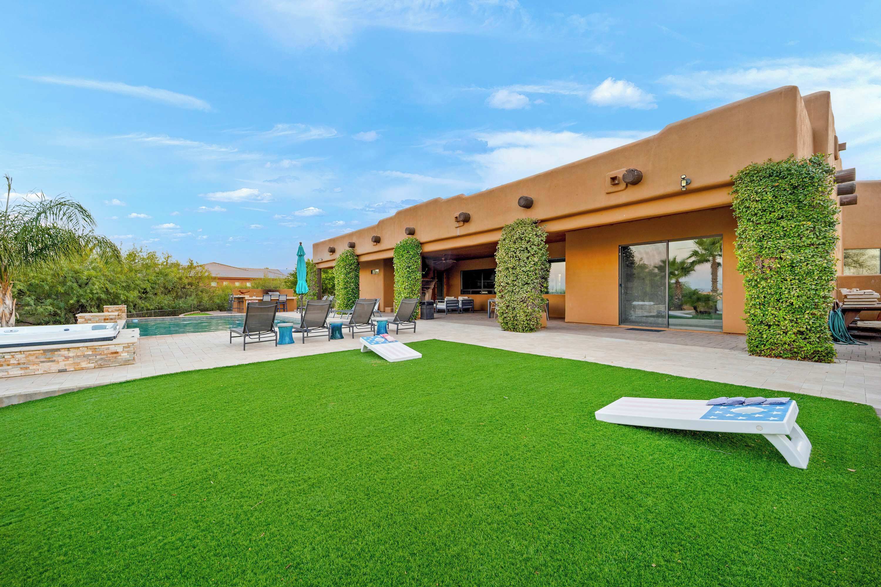 A pool area with artificial grass, lounge chairs, and a hot tub.