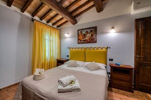 Ein Hotelzimmer mit einem Bett, einem Nachttisch, einem Gemälde und einer Holzbalkendecke.