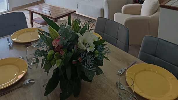 En stue med en sofa, et spisebord med gule tallerkener og en blomsteropsætning, en reol og et billede hængt på væggen.