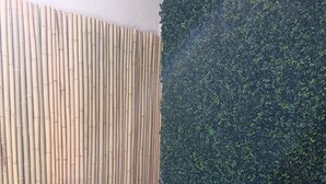 Et lille udendørs siddeområde med en bambusvæg og en væg dækket af grøn vegetation.