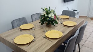 Spiseområde med et træbord, fire stole, gule tallerkener, bestik og en blomsteropsætning.