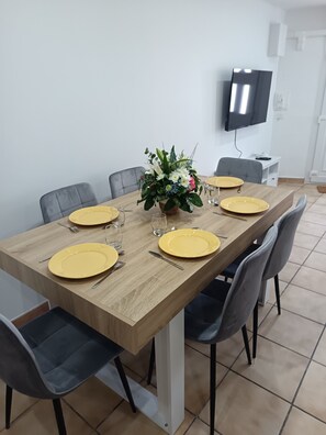 Un coin repas avec une table en bois, quatre chaises, des assiettes jaunes, des couverts et un centre de table floral.