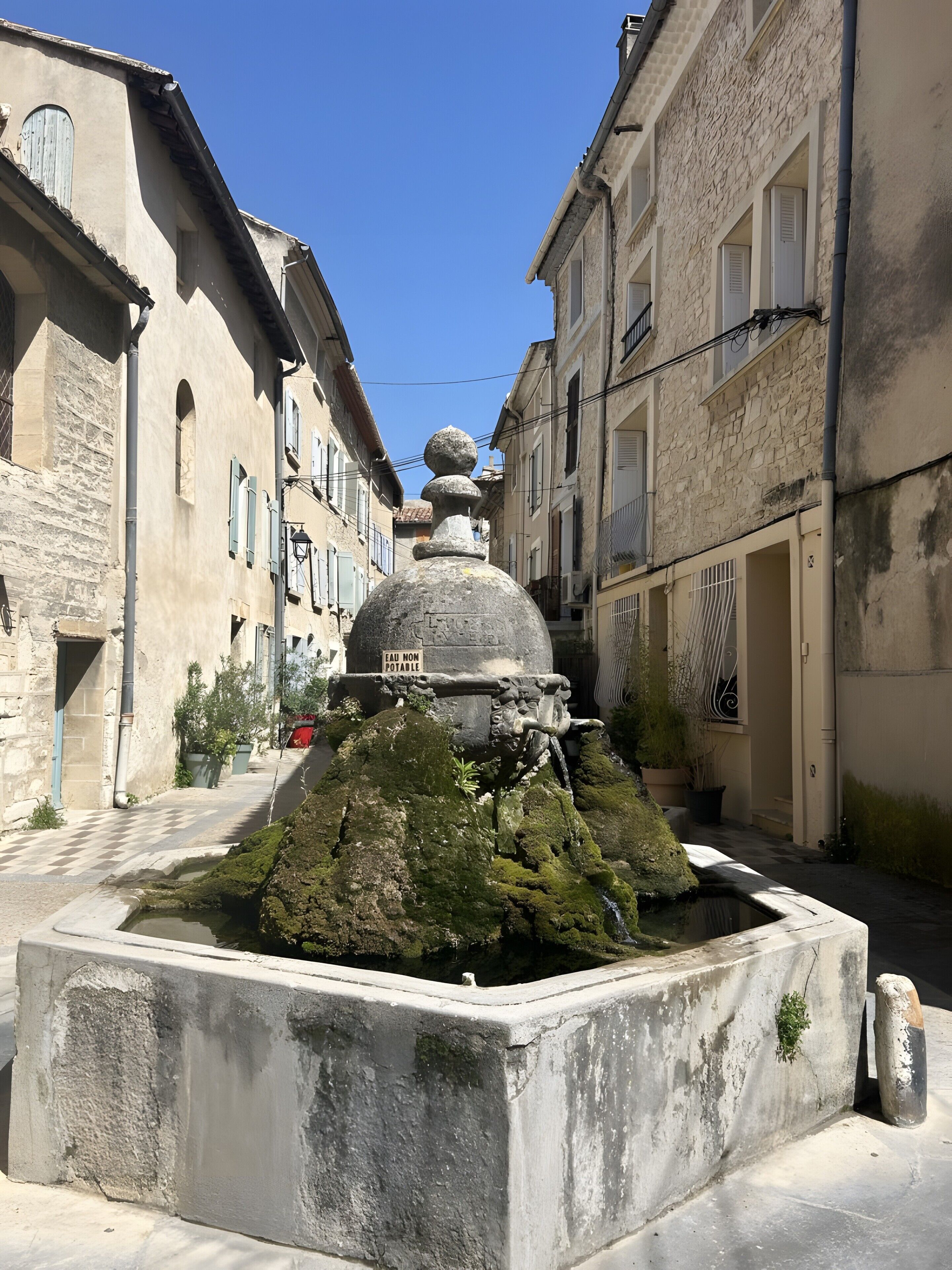 A stone fountain with a plaque, surrounded by old buildings with balconies and windows.