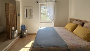 Een slaapkamer met een bed, een raam met gordijnen, een spiegel en een plafond met zichtbare balken.