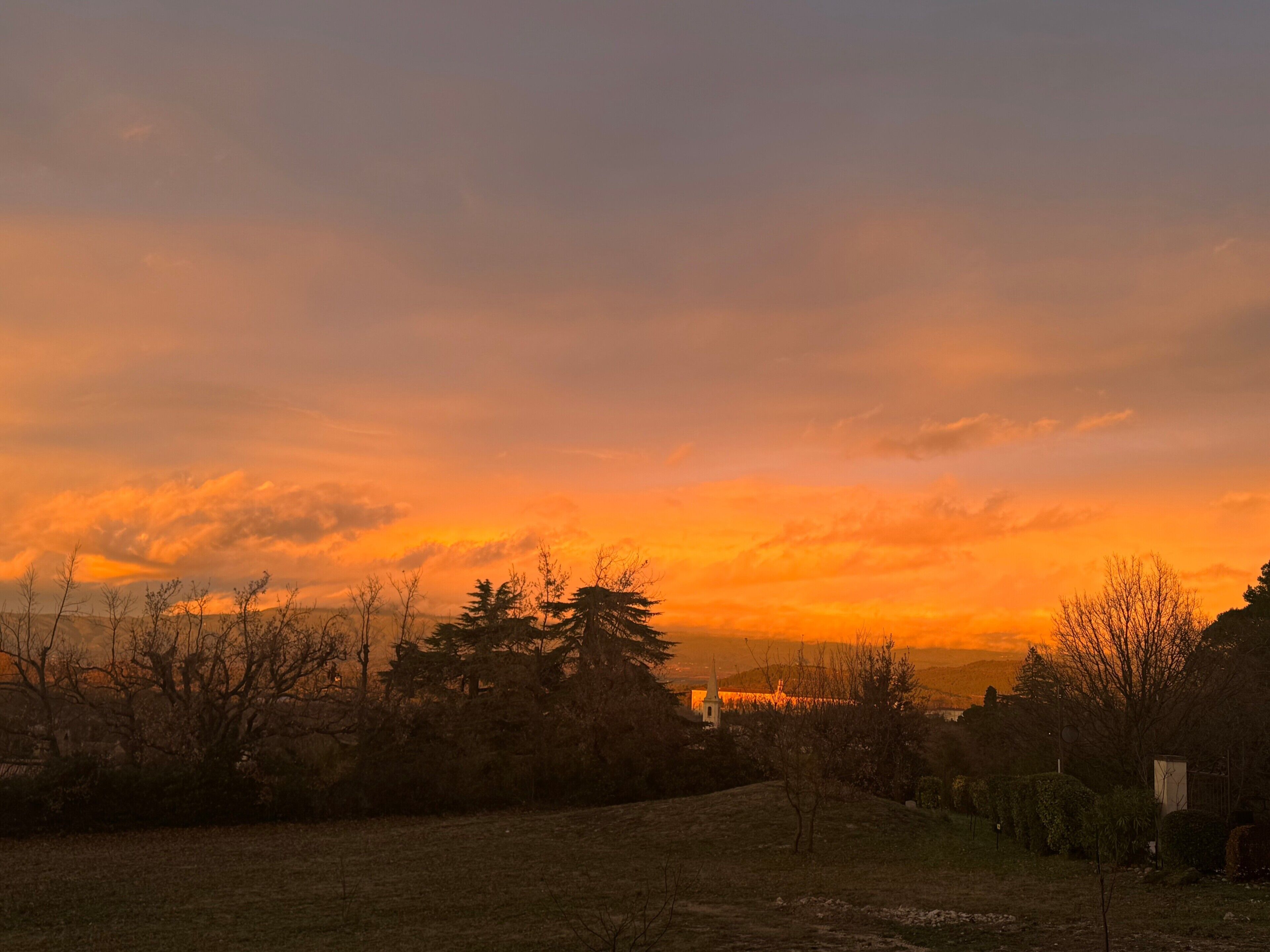 A sunset over a grassy field with trees and a distant building.