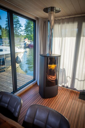 Ein Zimmer mit großem Fenster, Holzboden, Kamin und Blick auf Boote auf dem Wasser.