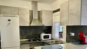 A modern kitchen with a refrigerator, microwave, stove, and a coffee maker. - Roses Apartment (Spain) with Sea and Mountain Views (Roses, Girona)