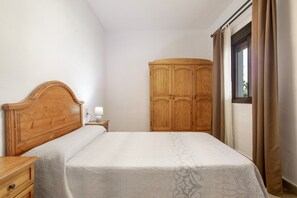 Een slaapkamer met een houten bed, een nachtkastje, een kledingkast en een raam met gordijnen.