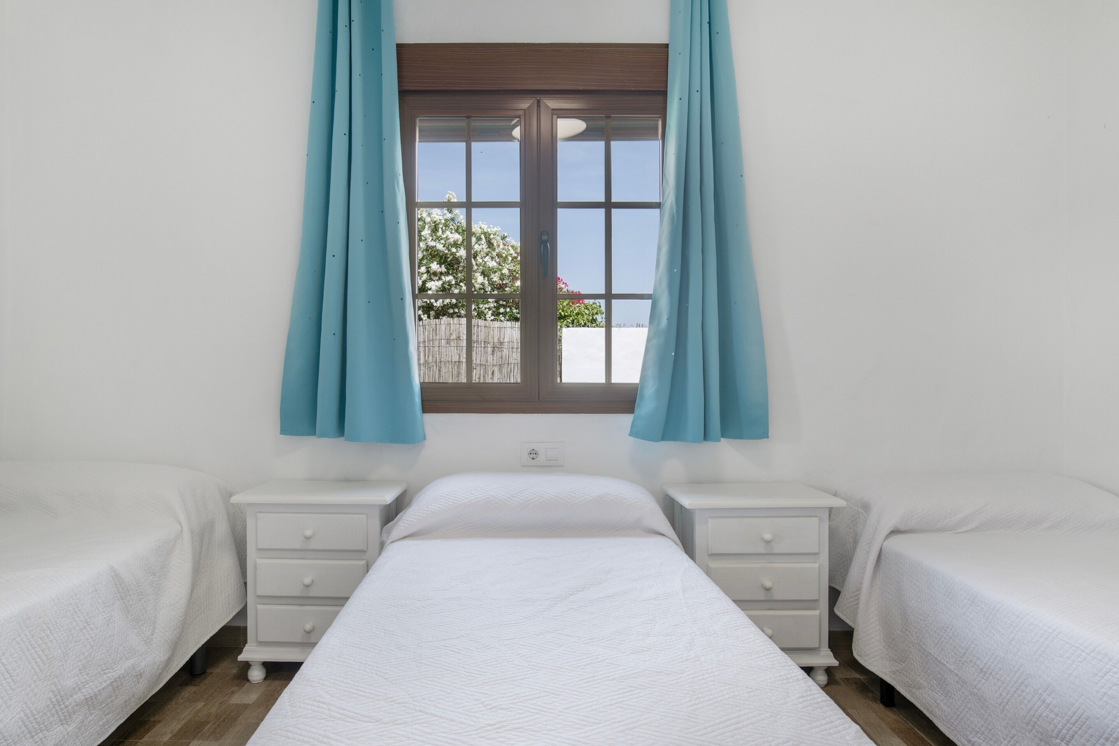 Een slaapkamer met twee eenpersoonsbedden, een raam met gordijnen en uitzicht op buiten.