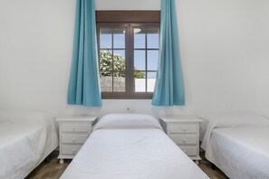 Un dormitori amb dos llits individuals, una finestra amb cortines i vista a l'exterior.