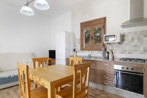 Een keuken met houten kastjes, een magnetron, een fornuis en een eettafel met stoelen.