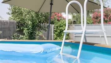 Een zwembad met een witte trap, een parasol en een houten terras.