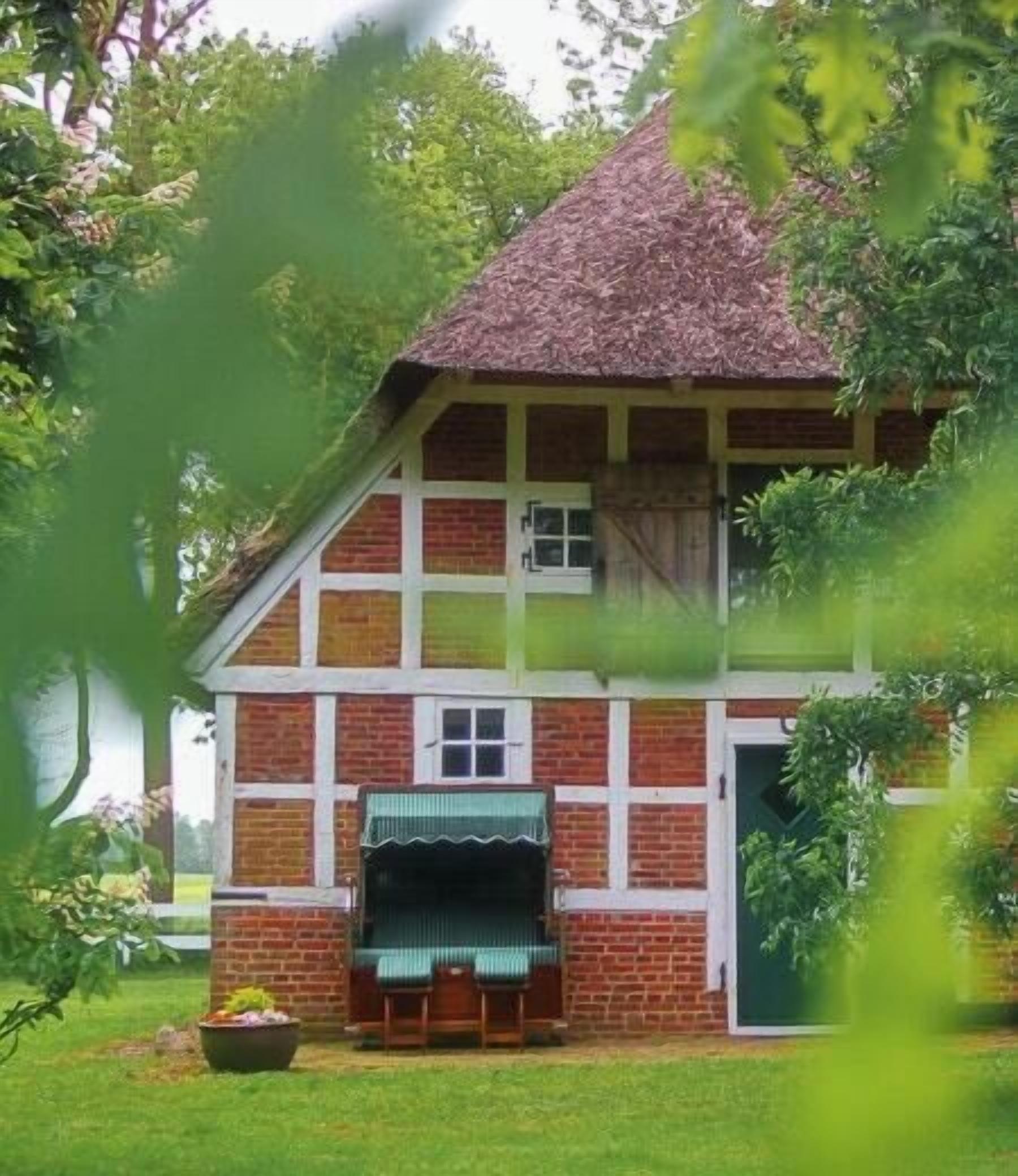 Ein traditionelles Haus mit einem Strohdach, einer Veranda mit Tisch und Stühlen und einer Ziegel Fassade.