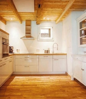 A kitchen with wooden ceiling beams, white cabinets, and a window above the sink. - Restored estate with sauna in Nordkehdingen (Oederquart)