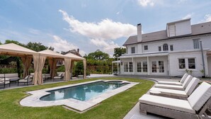 Un patio trasero con piscina, sillas de descanso y un área de patio techada.