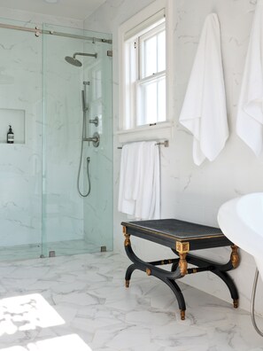 A bathroom with a glass shower enclosure, a white bathtub, a black vanity with gold accents, and a window providing natural light. - Boutique Estate with Private Pool, Gardens & Designer Interiors (Houston)