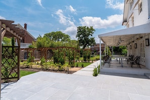 A patio area with a pergola, outdoor seating, and a brick building in the background. - Boutique Estate with Private Pool, Gardens & Designer Interiors (Houston)