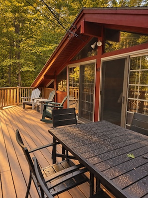 A wooden deck with outdoor furniture, including chairs and a table, and a building with a red roof and large windows. - Walk to Echo Lake • Sleeps 8 • Pet-Friendly Chalet (Conway)