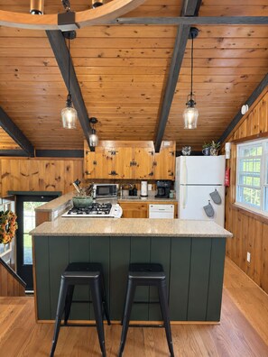 Een keuken met houten kastjes, een centraal eiland met krukken, een koelkast en hangende pendellampen.